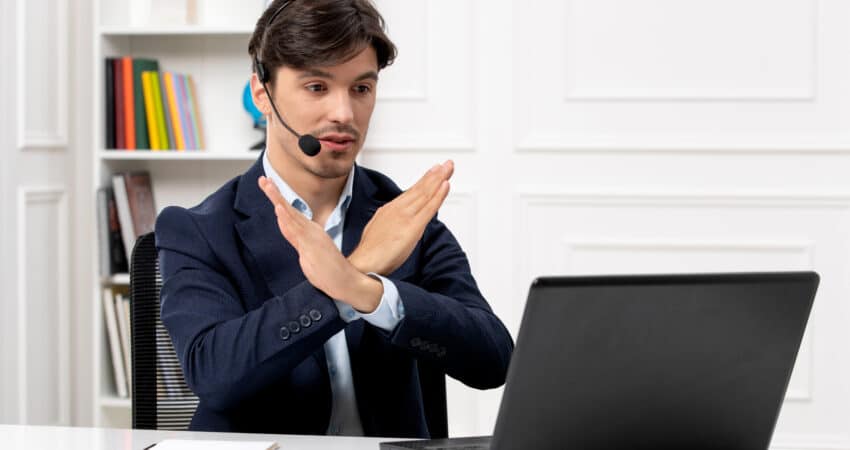 Customer support agent with headset showing stop gesture while using a laptop.