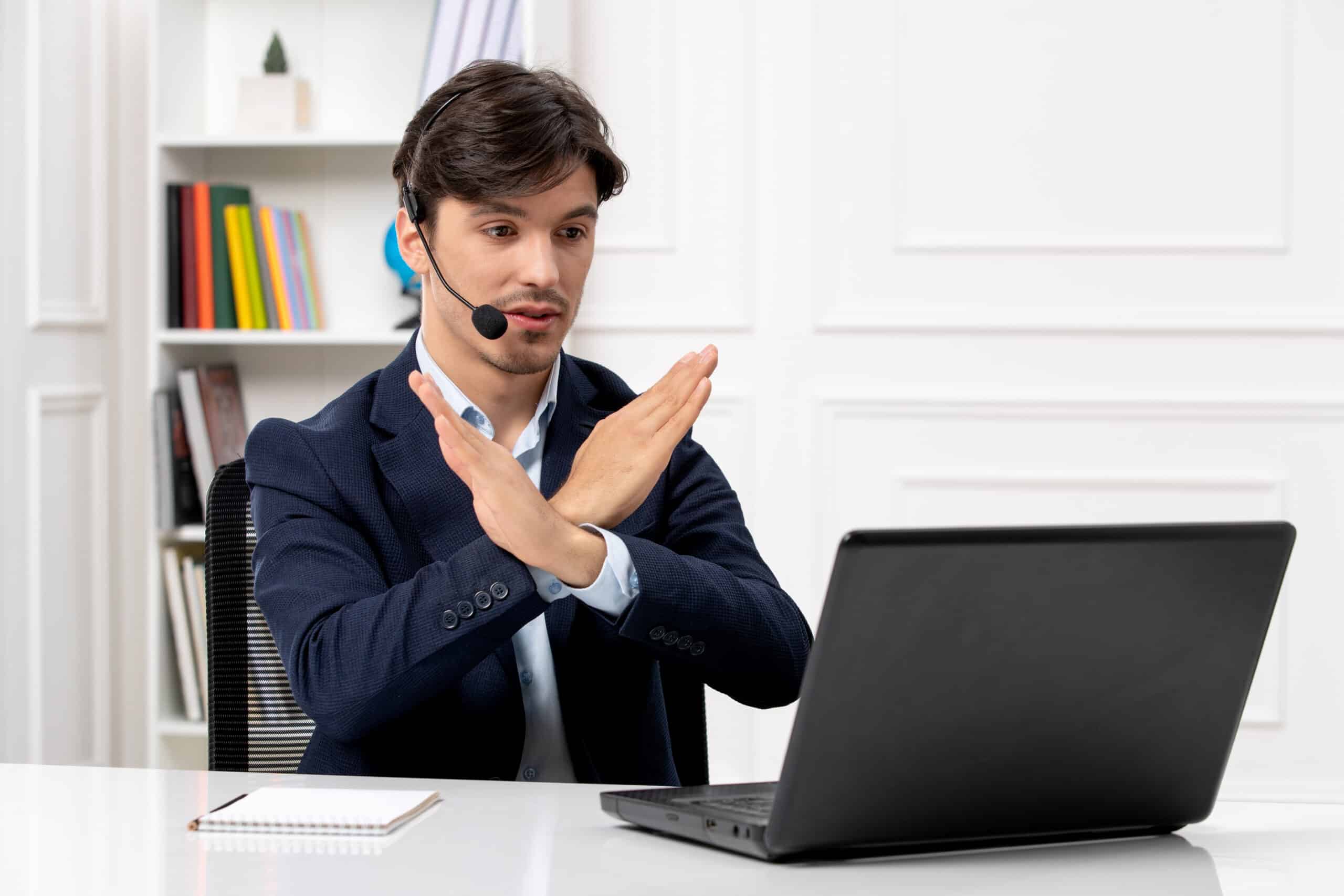 Customer support agent with headset showing stop gesture while using a laptop.