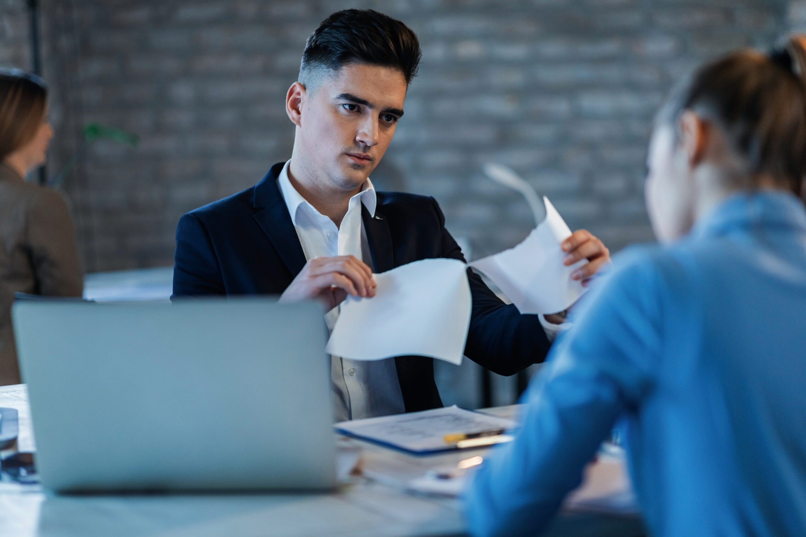 Man reviewing and tearing documents while discussing with a colleague in an office.